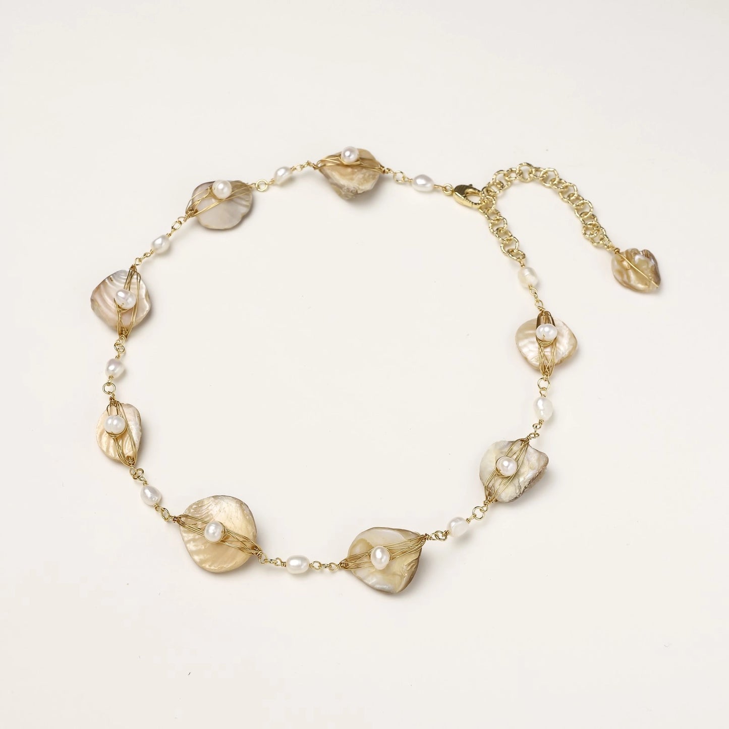 Delicate gold chain bracelet featuring iridescent shell charms with freshwater pearls on white background.