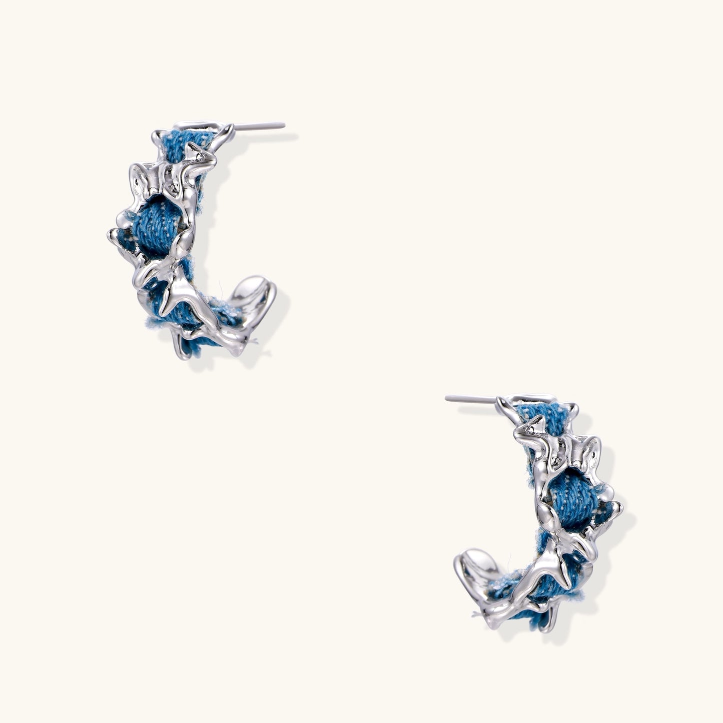 Crescent-shaped gold-plated hoop earrings with blue crystals set in organic vine-like metalwork on white background.