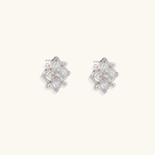 Detailed view of sterling silver stud earrings with geometric filigree design and small freshwater pearls on white background.