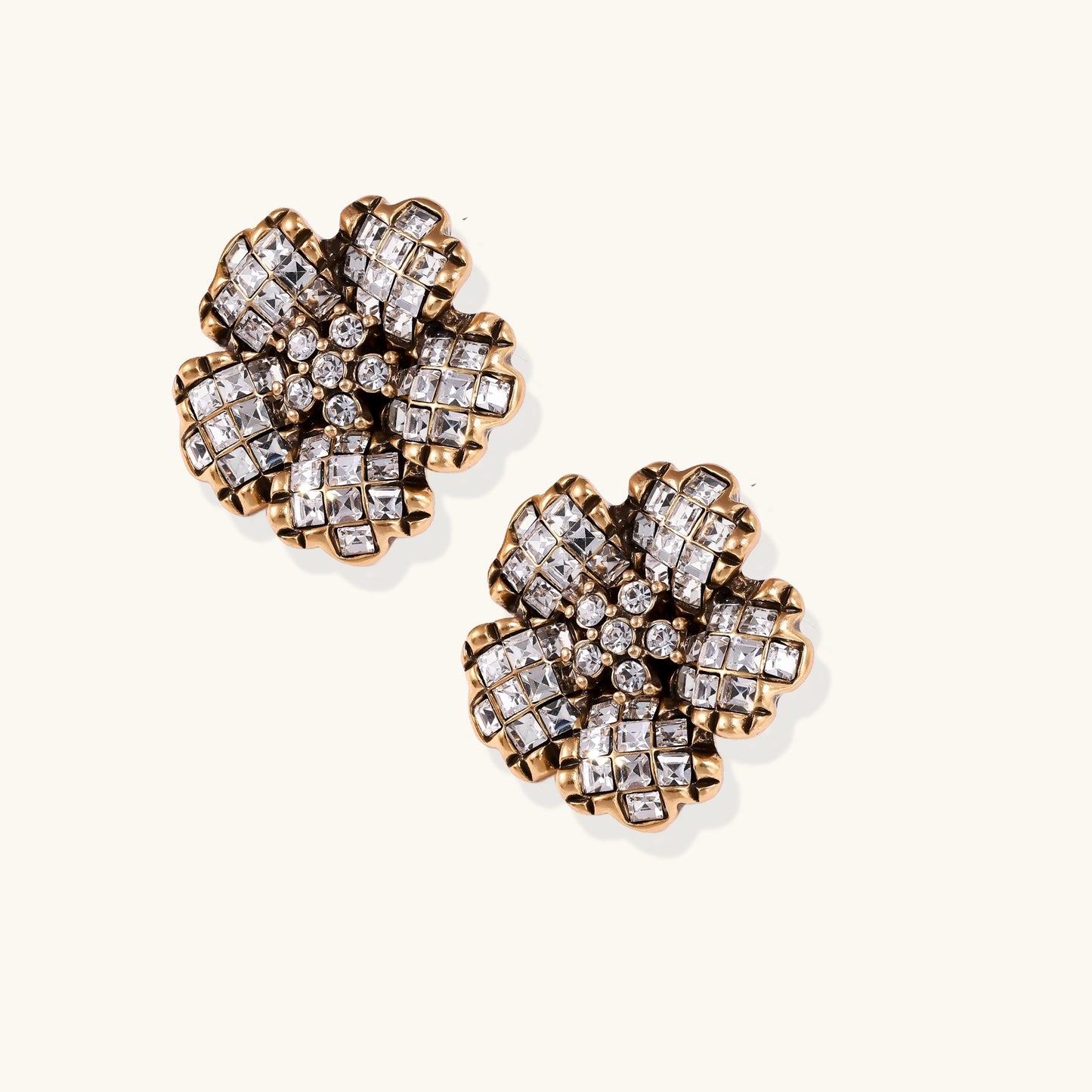 Ornate gold-plated flower earrings with clear zirconia crystals arranged in dimensional petal formations on cream background.