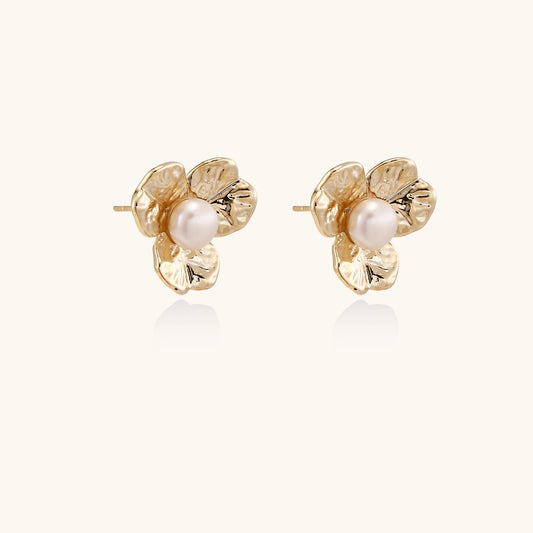 Gold-plated flower stud earrings with freshwater pearl centers on beige background, showing textured petal details.