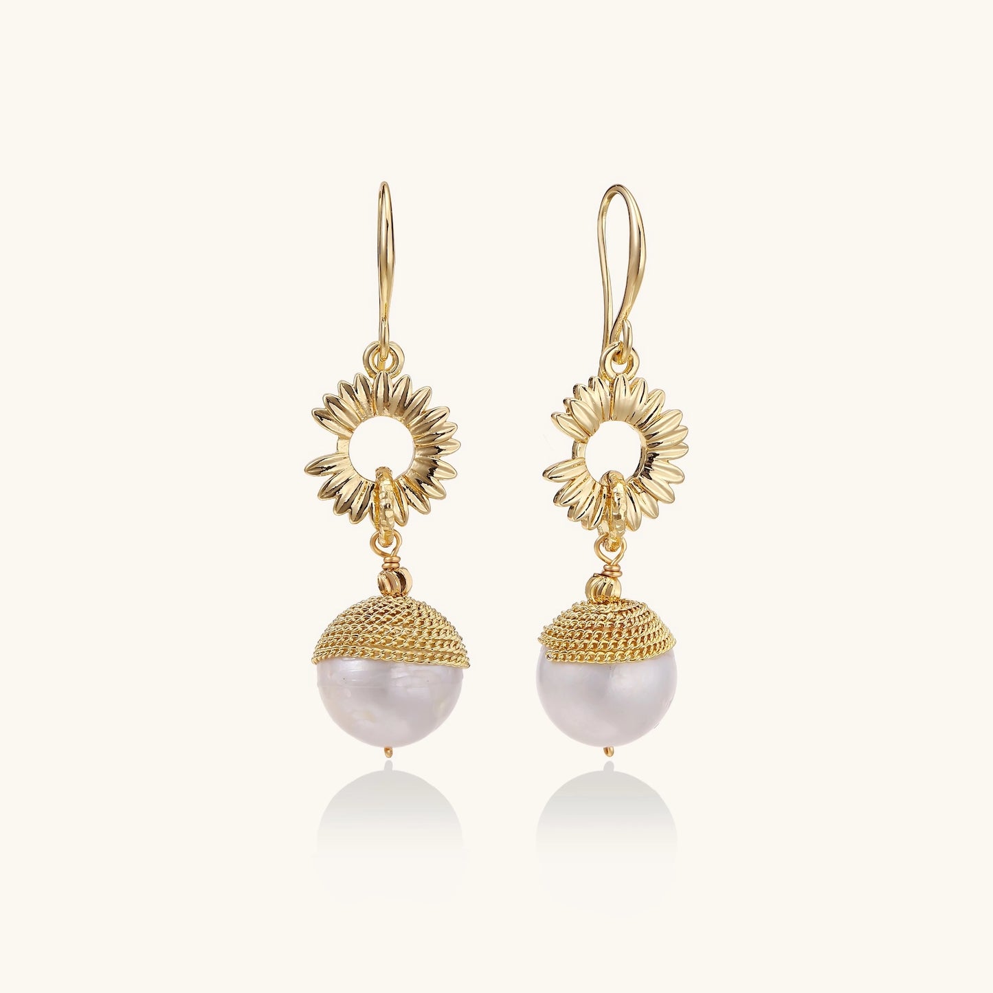 Gold-plated sunburst flower earrings with baroque pearl drops and textured metal caps on neutral background.