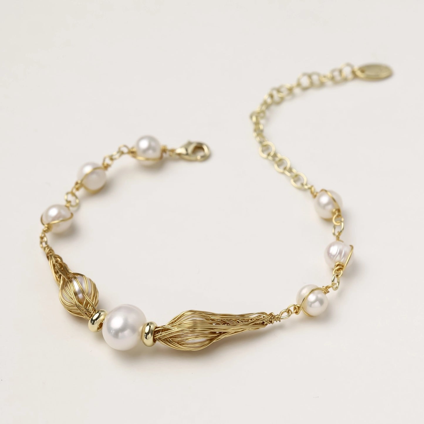 Delicate 14K gold plated bracelet with freshwater pearls and ribbed gold elements on cream background.