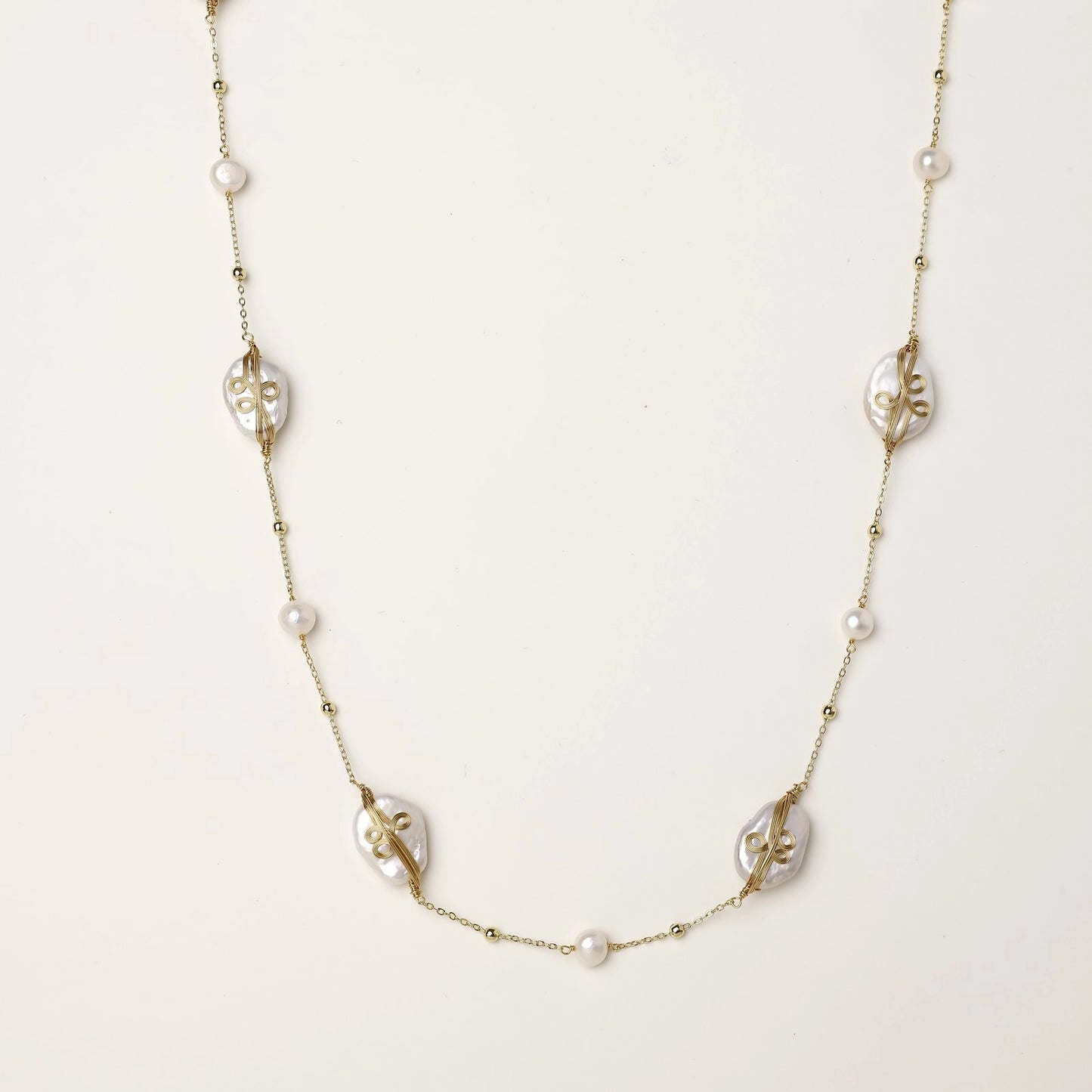 Delicate gold-plated necklace featuring translucent leaf-shaped baroque pearls and round freshwater pearls on neutral background.