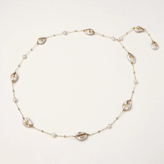 Delicate gold-plated necklace featuring translucent leaf-shaped baroque pearls and round freshwater pearls on neutral background.