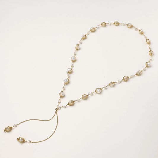 Long gold-plated lariat necklace with wire-wrapped freshwater pearls and chain tassel detail on cream background.