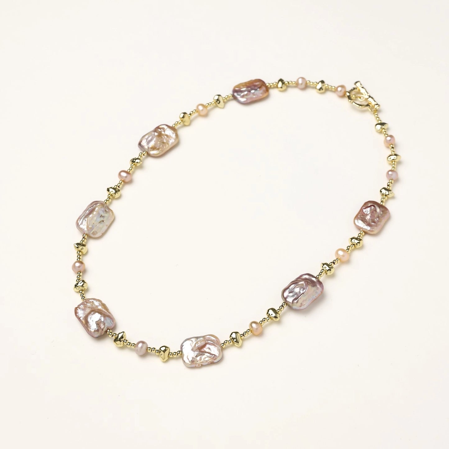 Long gold-plated necklace with iridescent baroque pearls and round freshwater pearls on cream background