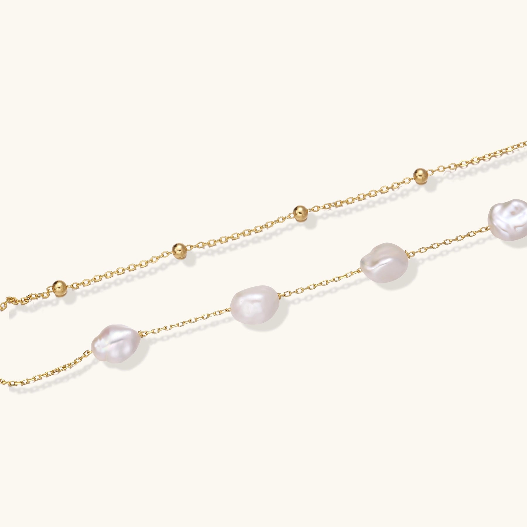 Delicate multi-layered gold-plated bracelet with irregular baroque pearls and freshwater pearls on cream background.