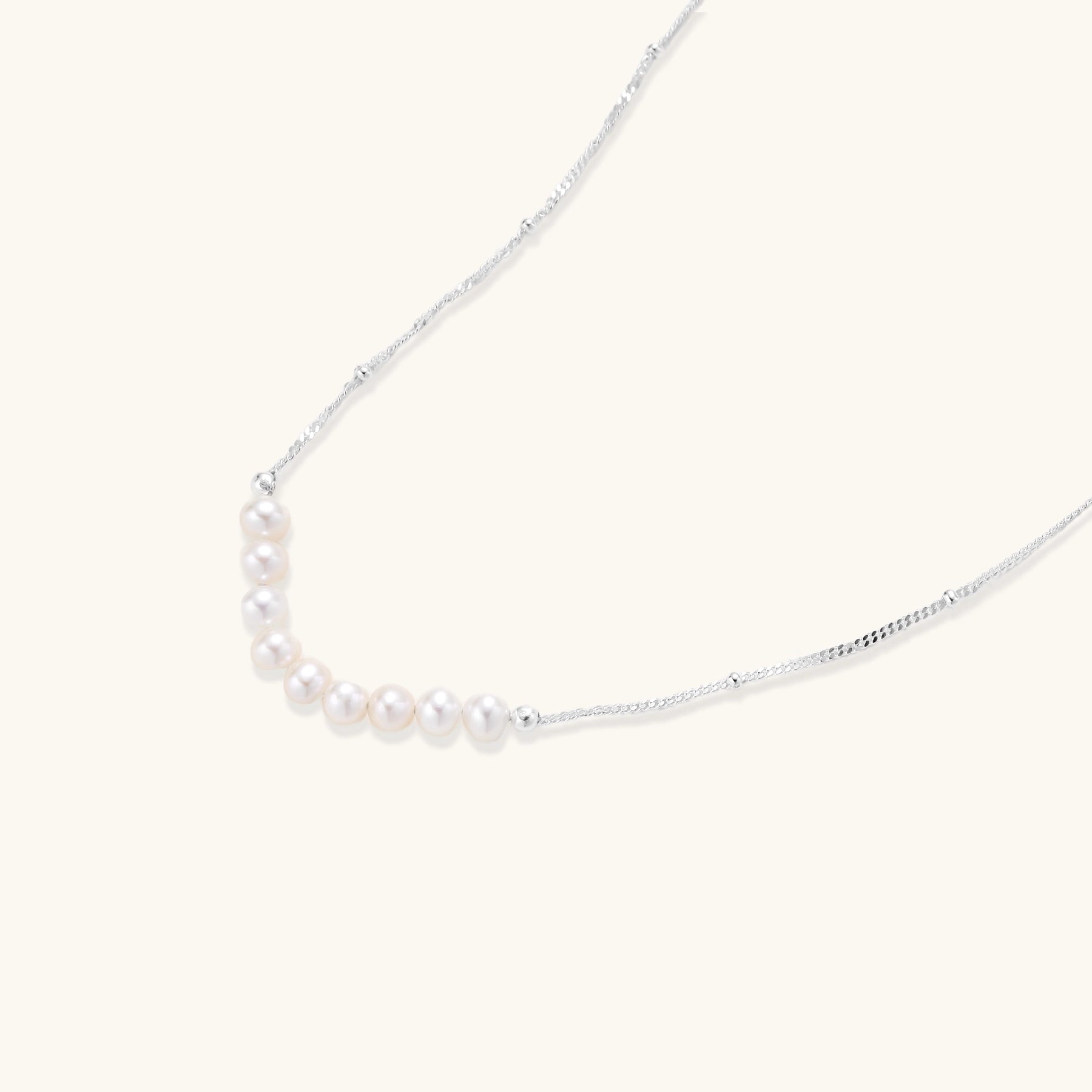 Delicate sterling silver chain with small white freshwater pearls arranged asymmetrically on white background.