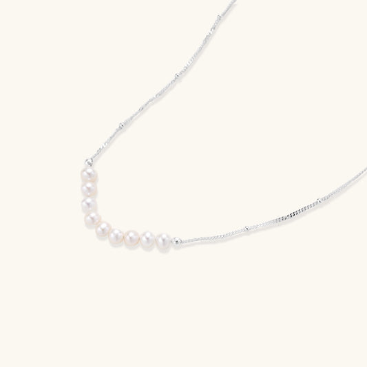 Delicate sterling silver chain with small white freshwater pearls arranged asymmetrically on white background.