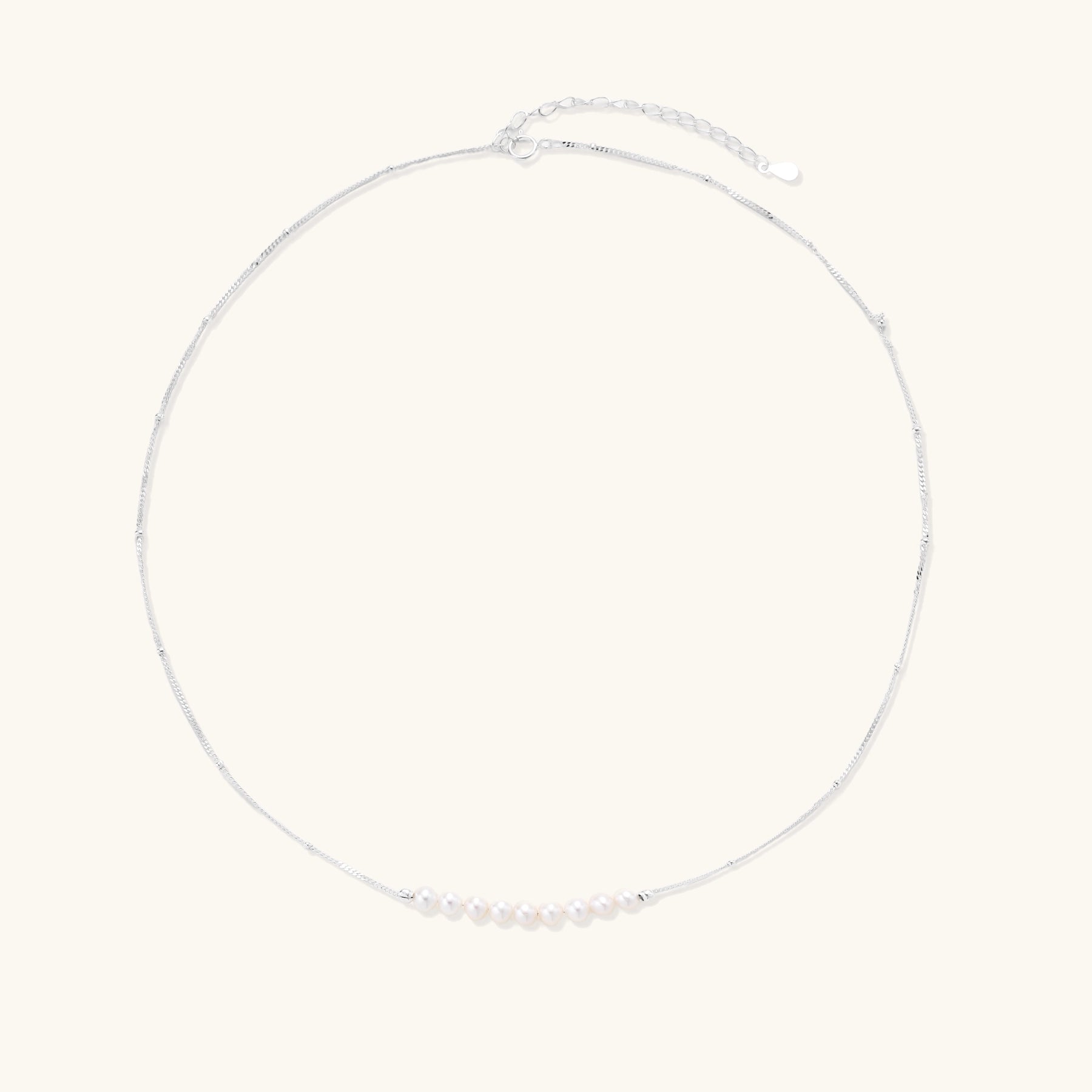 Delicate sterling silver chain with small white freshwater pearls arranged asymmetrically on white background.