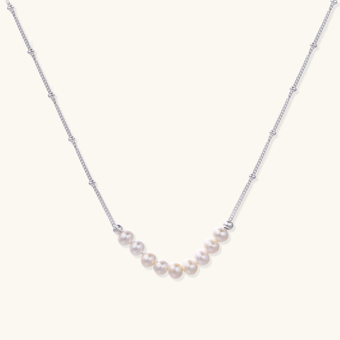 Delicate sterling silver chain with small white freshwater pearls arranged asymmetrically on white background.