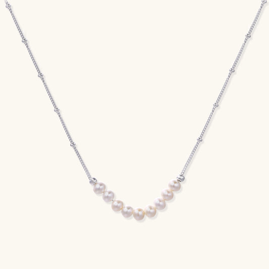 Delicate sterling silver chain with small white freshwater pearls arranged asymmetrically on white background.