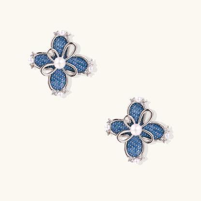 Blue denim flower stud earrings with silver framework, white pearl centers, and crystal accents on cream background.