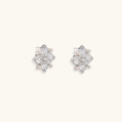 Detailed view of sterling silver stud earrings with geometric filigree design and small freshwater pearls on white background.