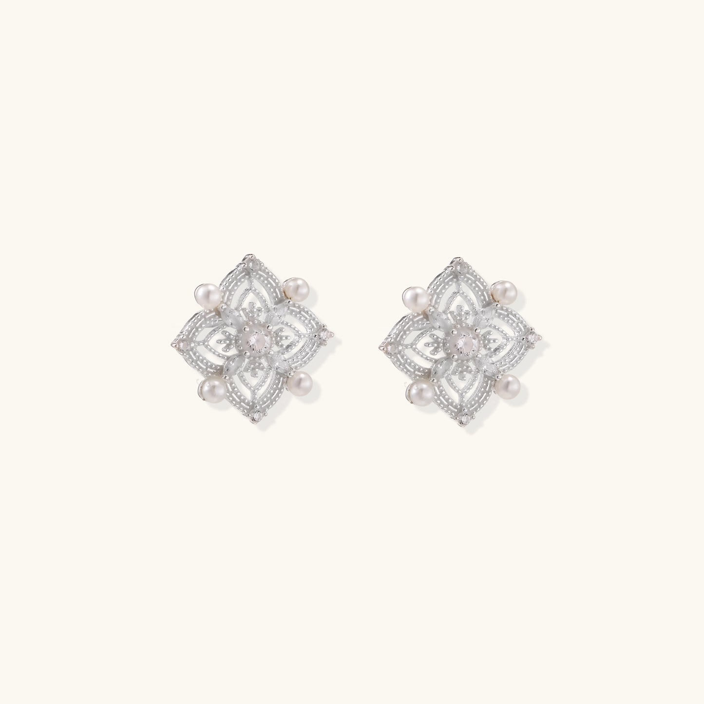 Detailed view of sterling silver stud earrings with geometric filigree design and small freshwater pearls on white background.