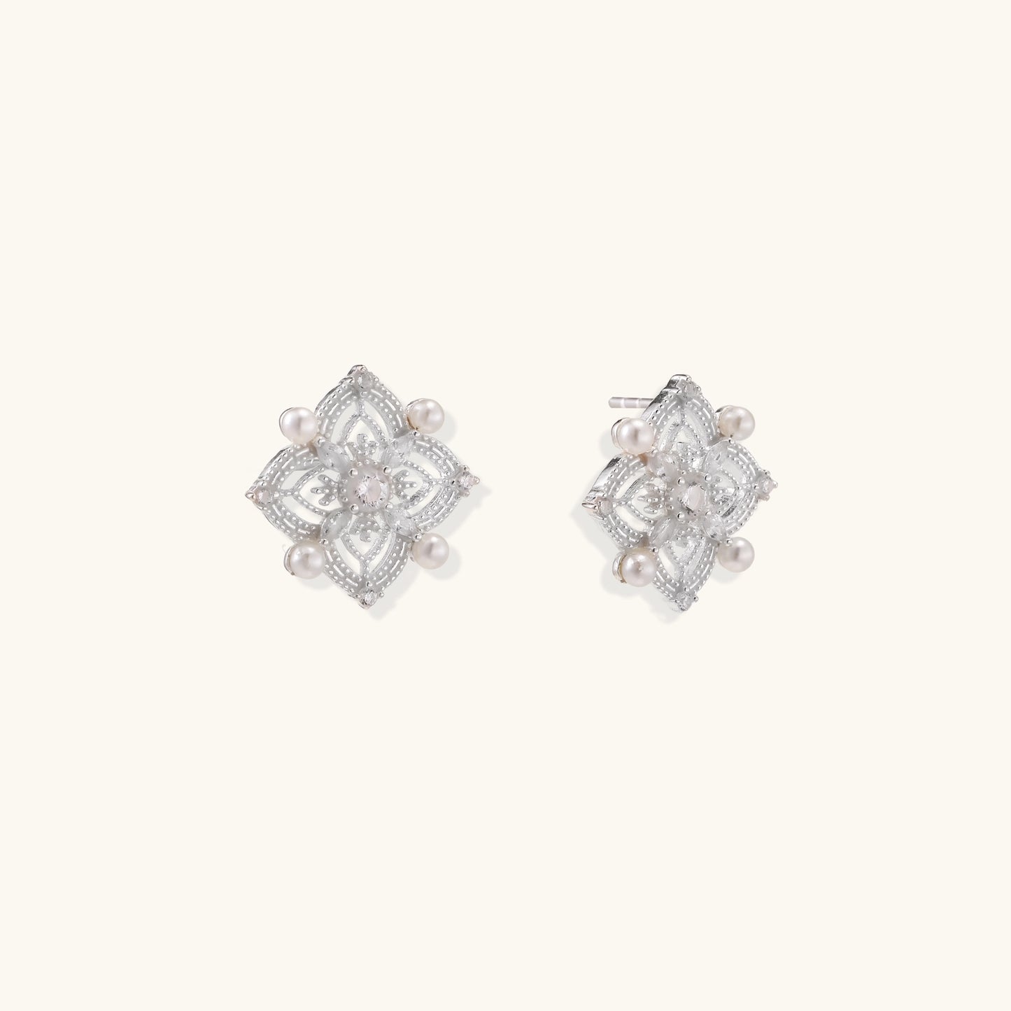 Detailed view of sterling silver stud earrings with geometric filigree design and small freshwater pearls on white background.