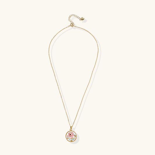 Gold-plated circular pendant featuring pink enamel rose with pearl accents and green leaf details on adjustable chain.