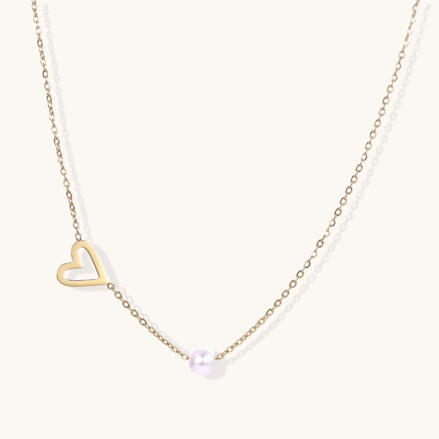 Dainty 14K gold-plated necklace with open heart pendant and white pearl bead on neutral background