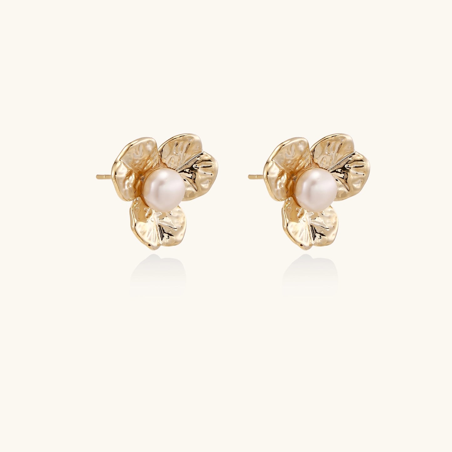 Gold-plated flower stud earrings with freshwater pearl centers on beige background, showing textured petal details.