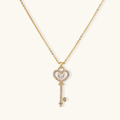 Gold-plated key pendant necklace with heart top and crystal embellishments on adjustable chain against cream background