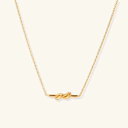 Dainty 18K gold plated stainless steel chain necklace with minimalist knot pendant on cream background.