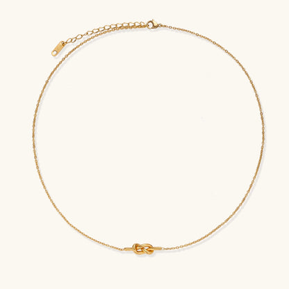 Dainty 18K gold plated stainless steel chain necklace with minimalist knot pendant on cream background.