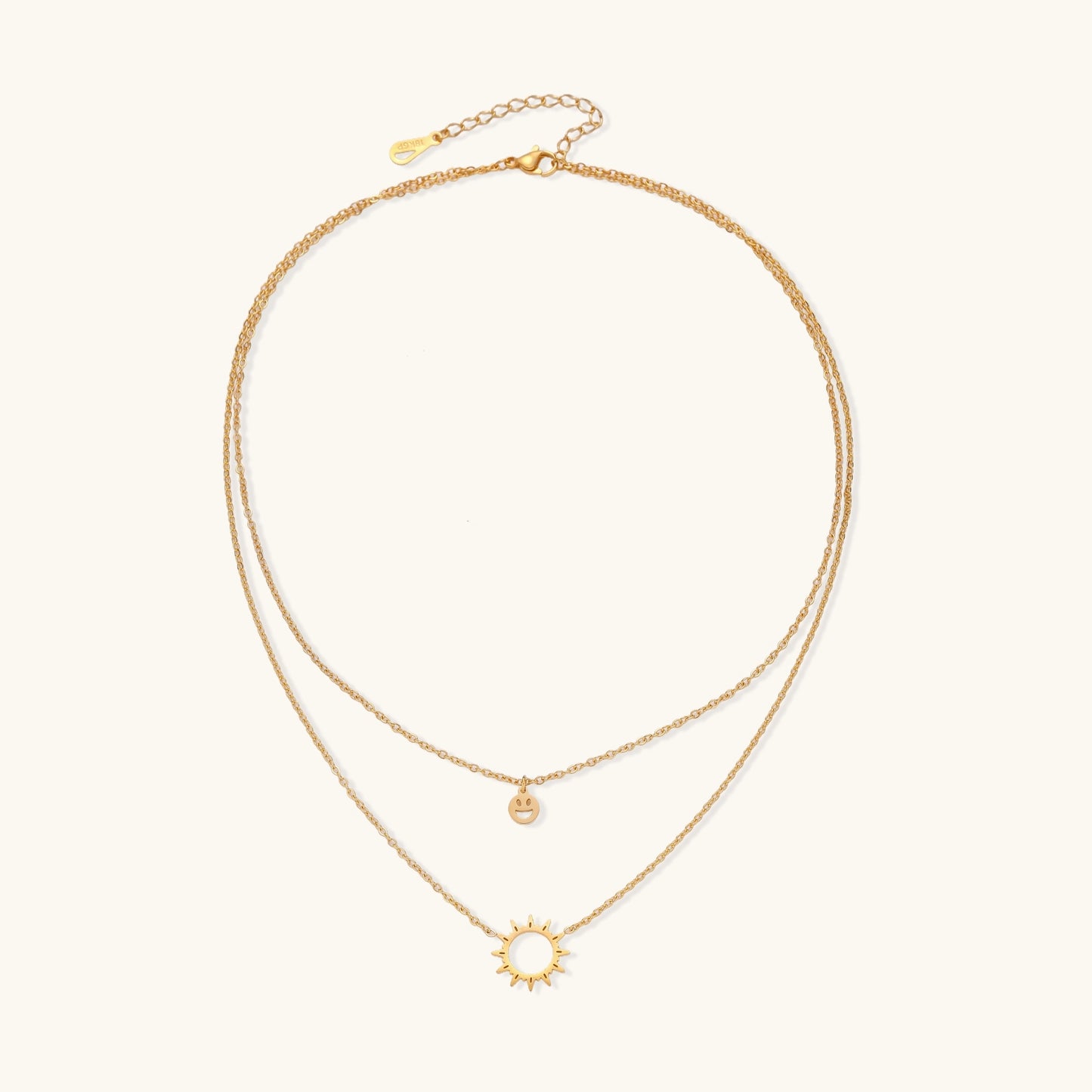 Delicate gold-plated layered necklace with smiley face and sun pendants on white background, showing adjustable chain.