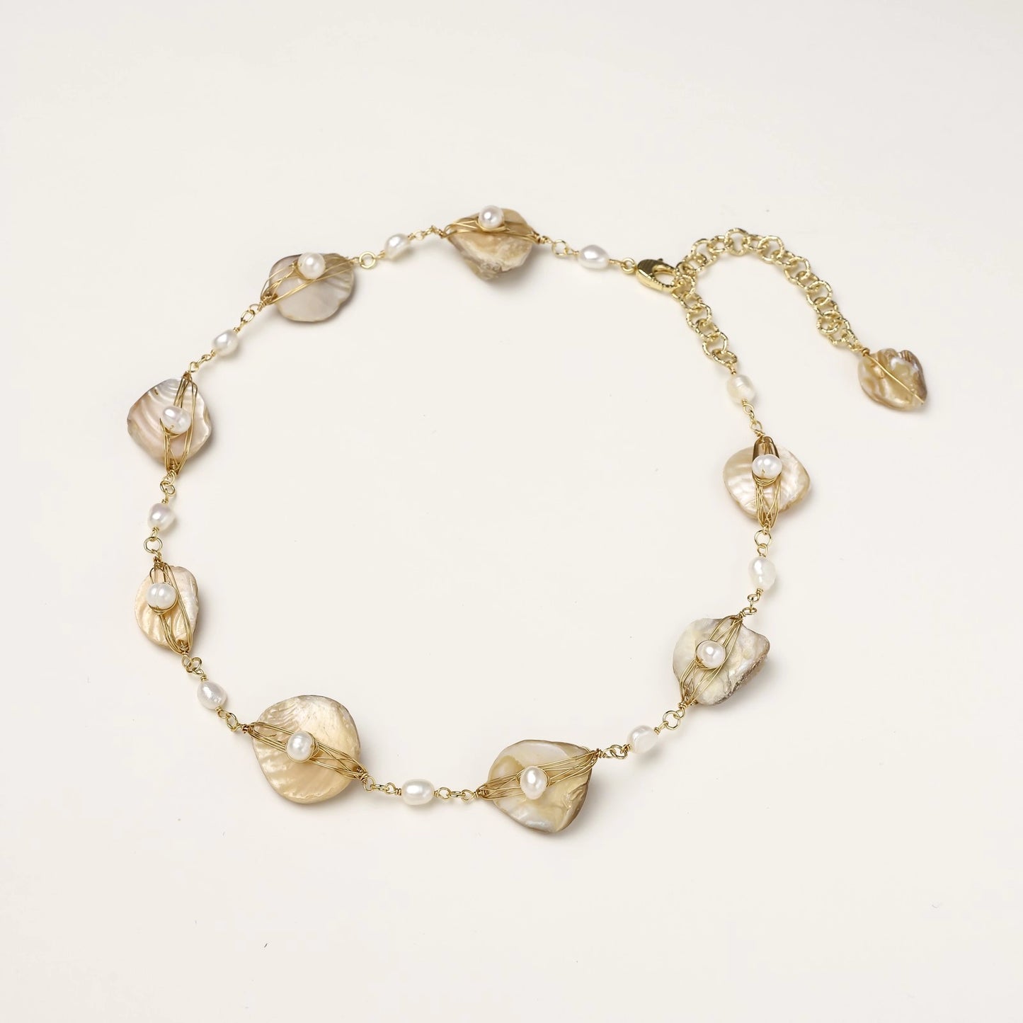 Gold-plated necklace with wire-wrapped shell pieces and freshwater pearls on neutral background, adjustable chain visible.