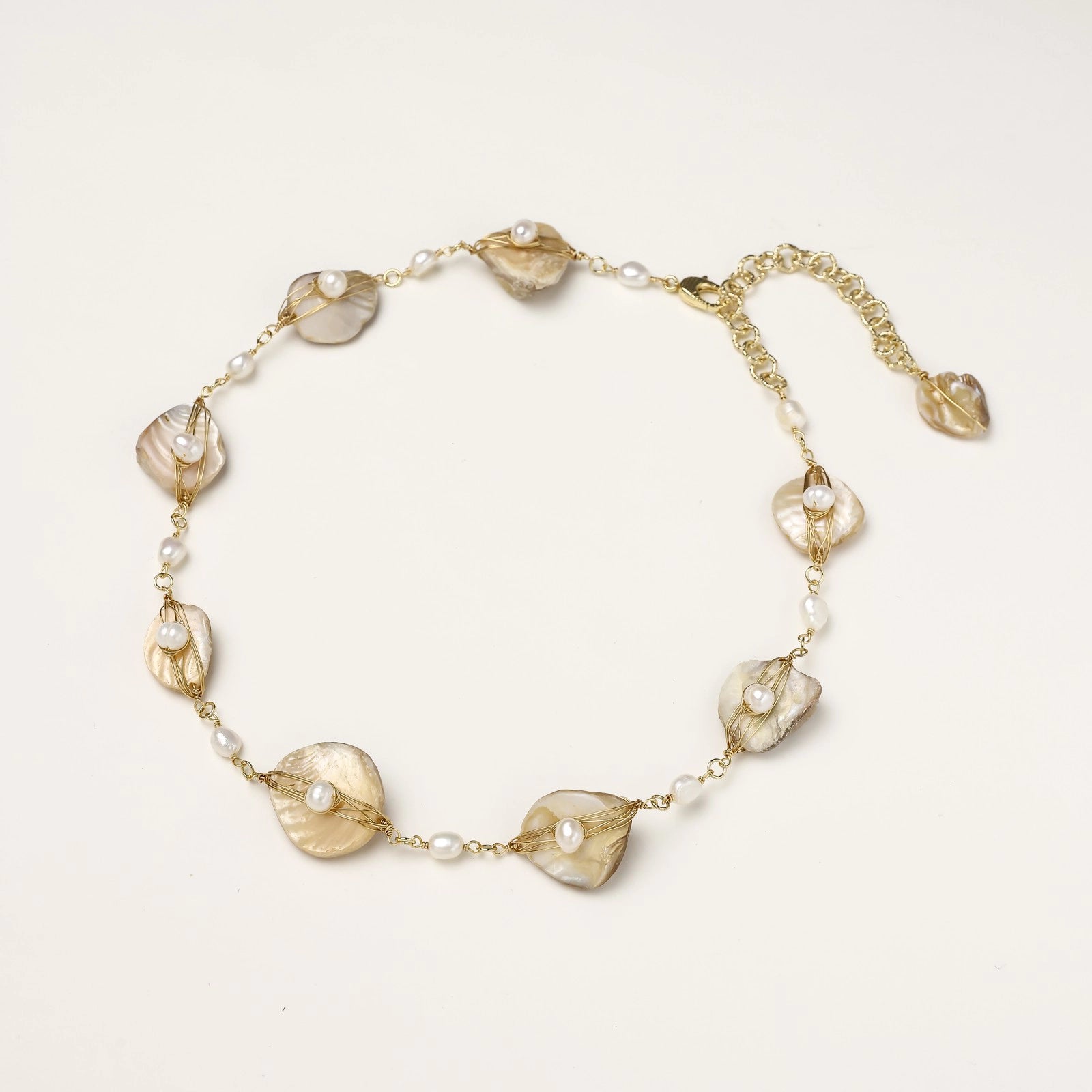 Gold-plated necklace with wire-wrapped shell pieces and freshwater pearls on neutral background, adjustable chain visible.