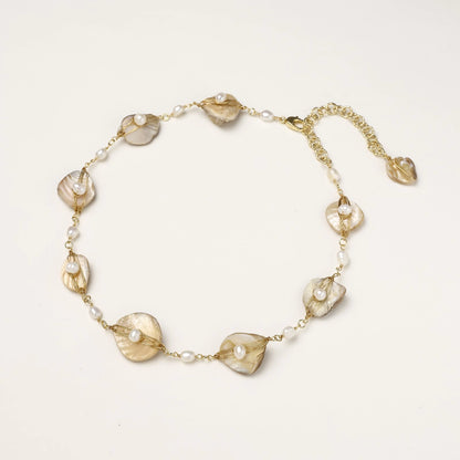 Gold-plated necklace with wire-wrapped shell pieces and freshwater pearls on neutral background, adjustable chain visible.