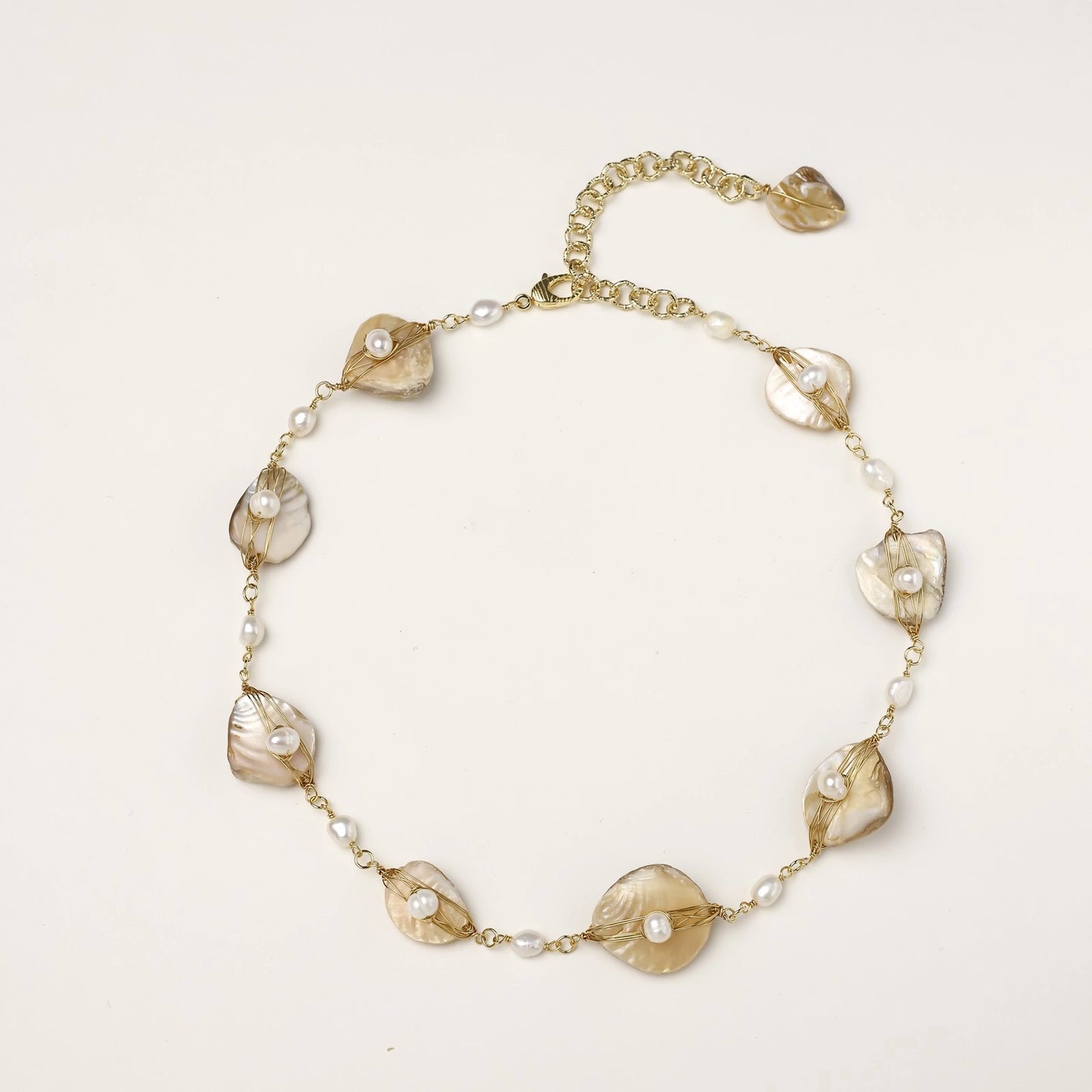 Gold-plated necklace with wire-wrapped shell pieces and freshwater pearls on neutral background, adjustable chain visible.