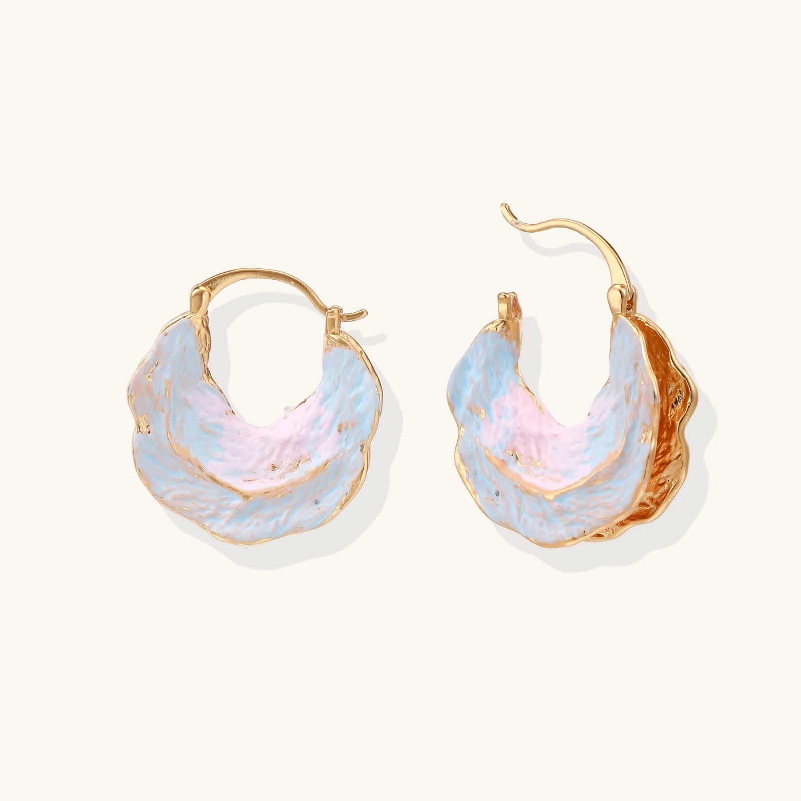 Shell-shaped hoop earrings with iridescent blue-pink enamel and gold trim on cream background