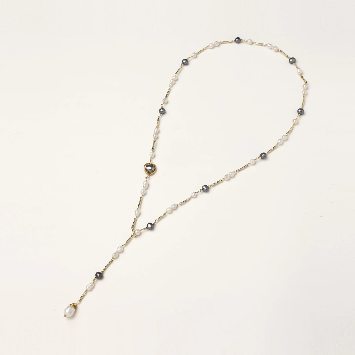 Y-shaped gold-plated necklace with white and gray freshwater pearls on cream background, showing adjustable drop design.