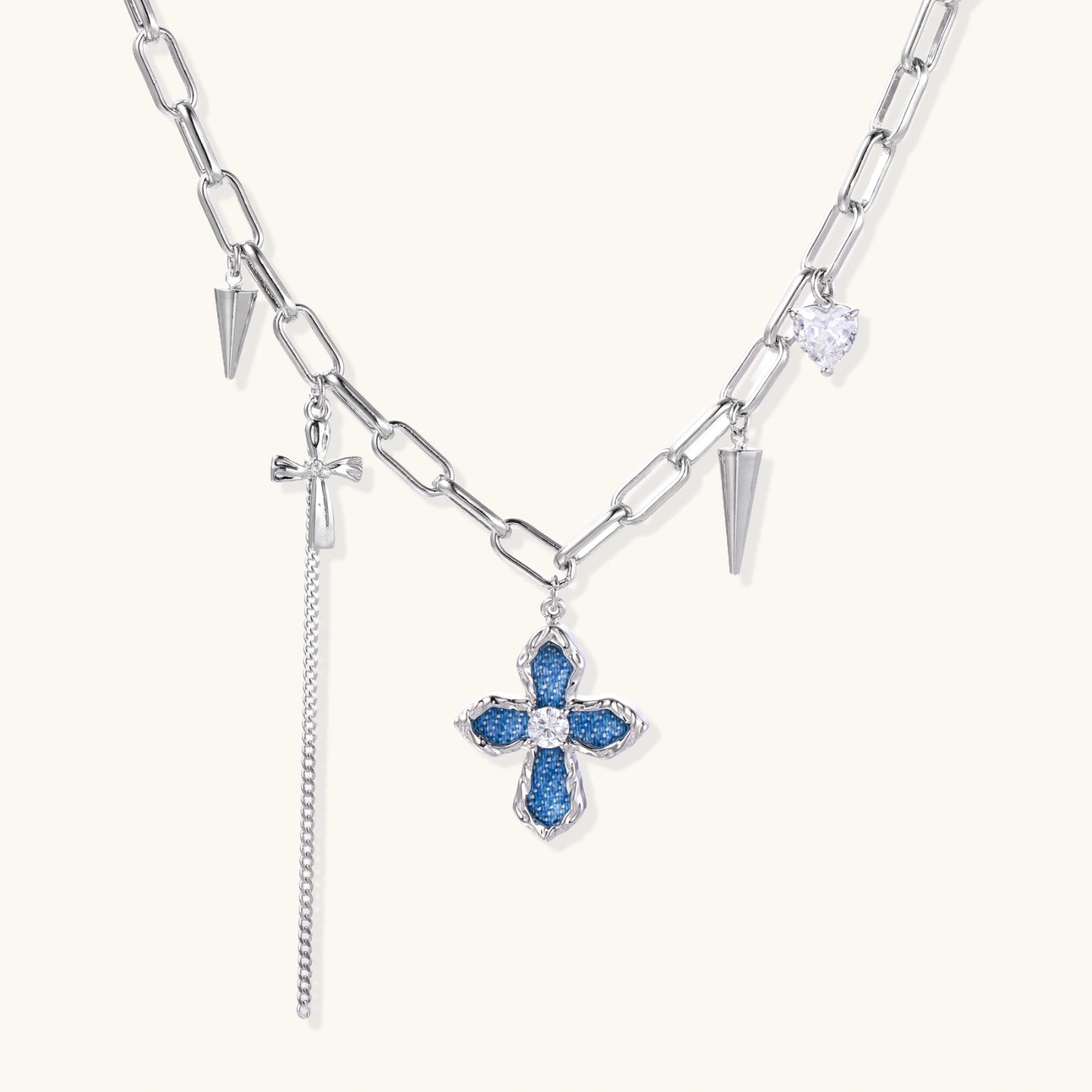 White gold plated chain necklace with blue textured cross pendant, spike charms, and mini cross detail on beige background