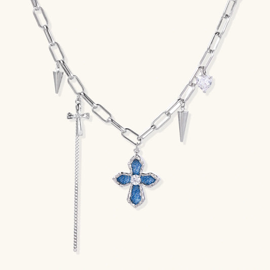 White gold plated chain necklace with blue textured cross pendant, spike charms, and mini cross detail on beige background