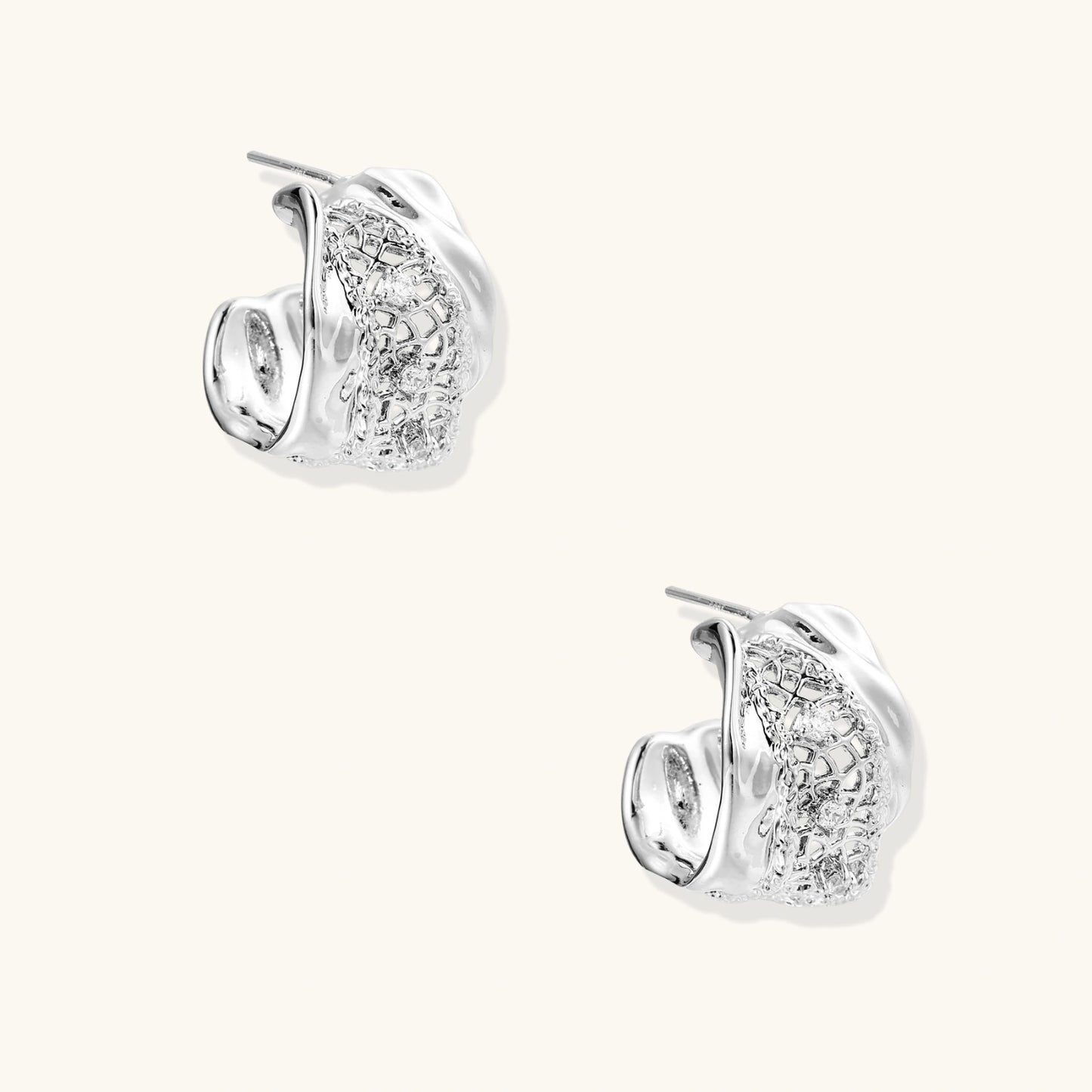 Close-up of sculptural hoop earrings with lattice center band and smooth twisted edges in white gold-plated brass with zirconia