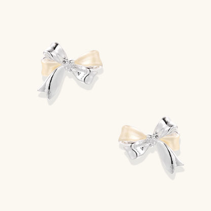Dimensional bow stud earrings in white gold plated brass with silver and cream two-tone finish on neutral background