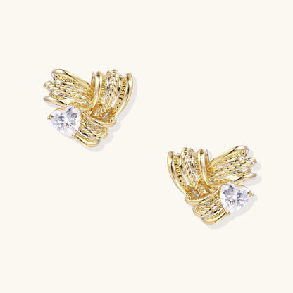 Pair of sculptural gold-plated wing stud earrings with zirconia stones on cream background, showing dimensional feather design