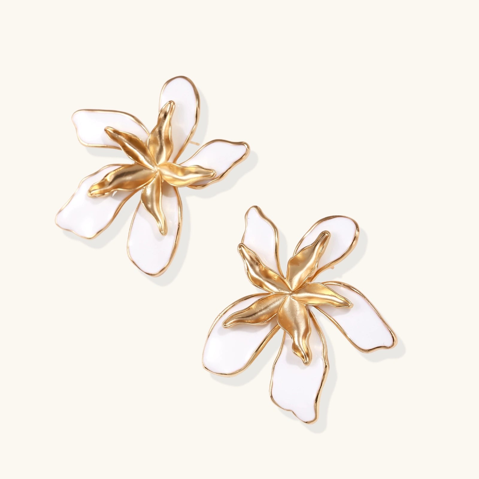 White enamel tropical flower earrings with sculptural gold-plated center and organic petal design on cream background