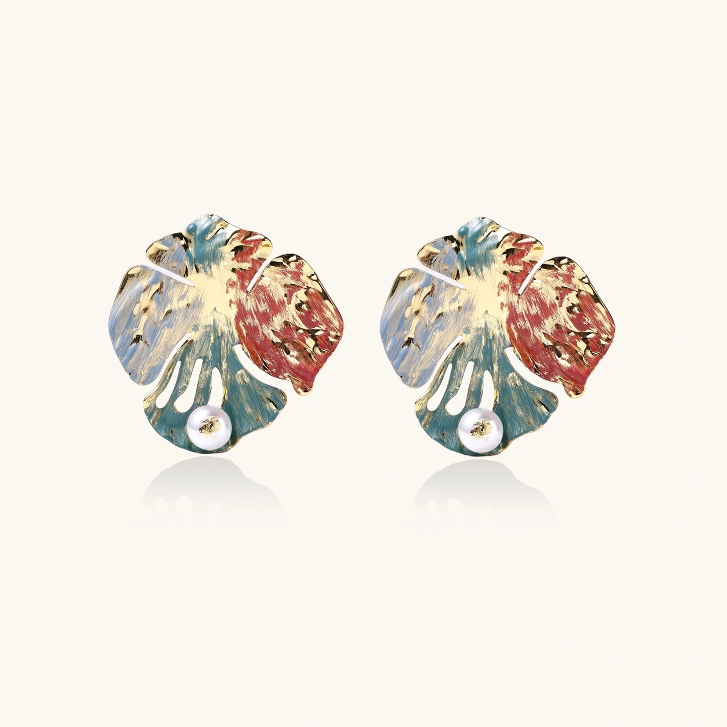 Artistic monstera-shaped earrings with teal, coral, and cream enamel brushstrokes, gold trim, and white pearl accent