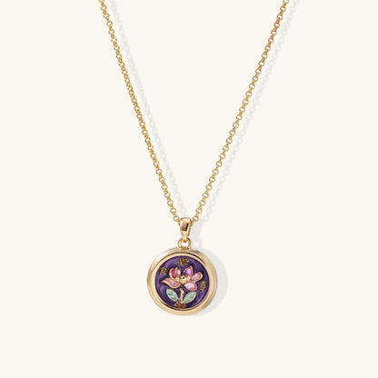 Gold-plated circular pendant with hand-painted purple enamel floral design on delicate chain against cream background