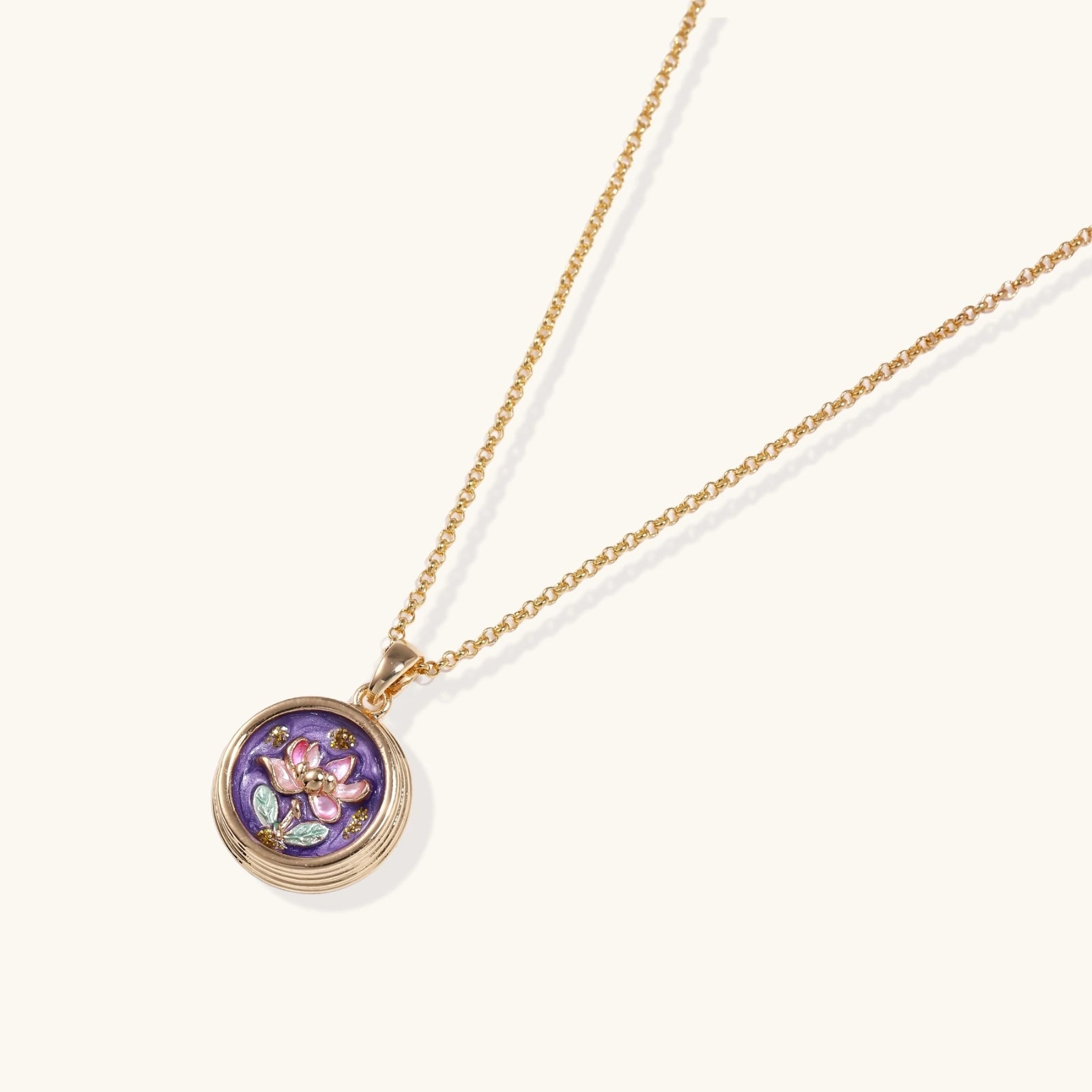 Gold-plated circular pendant with hand-painted purple enamel floral design on delicate chain against cream background