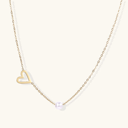 Delicate gold necklace with open heart charm and white pearl bead on fine chain against cream background