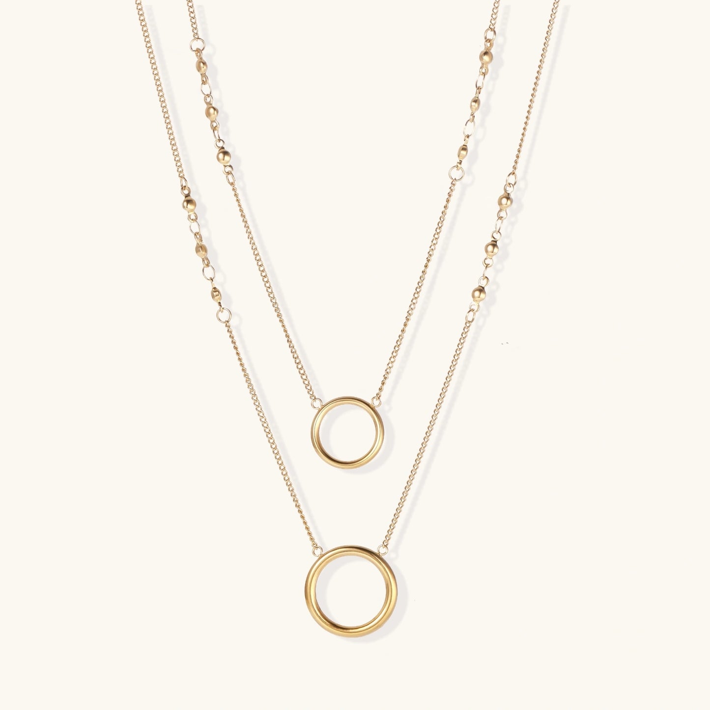 Layered gold necklace set with two open circle pendants and mixed chain styles on beige background