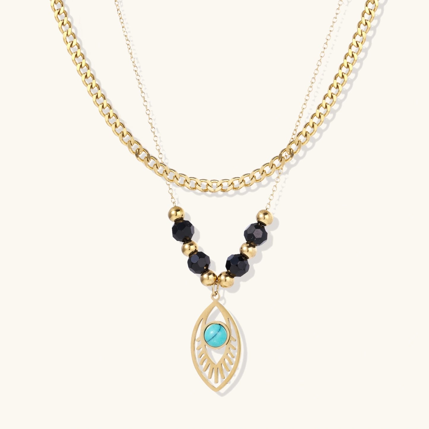Layered gold necklace with turquoise evil eye pendant and black quartz beads on cream background