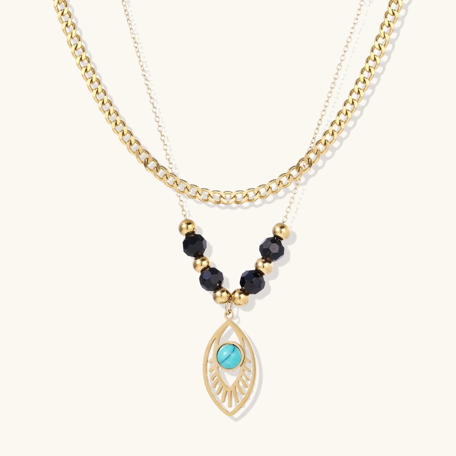 Layered gold necklace with turquoise evil eye pendant and black quartz beads on cream background