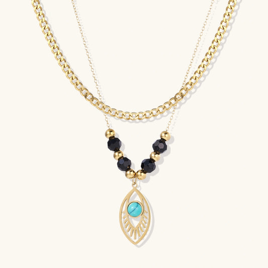 Layered gold necklace with turquoise evil eye pendant and black quartz beads on cream background