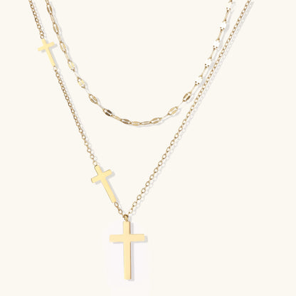 Three-layered gold necklace set with graduated cross pendants in mixed chain styles on white background.