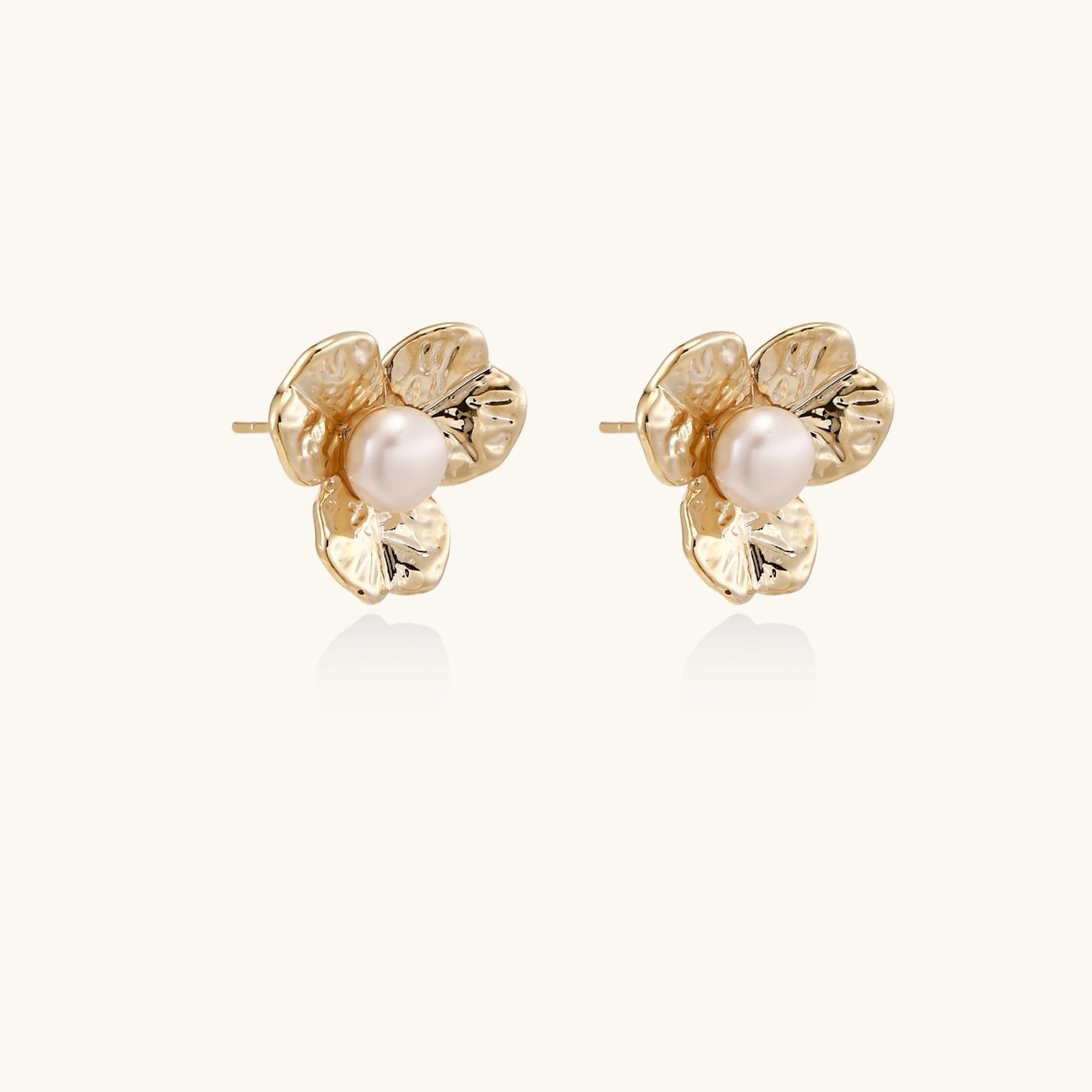 Gold-plated flower stud earrings with textured petals and centered freshwater pearl on beige background
